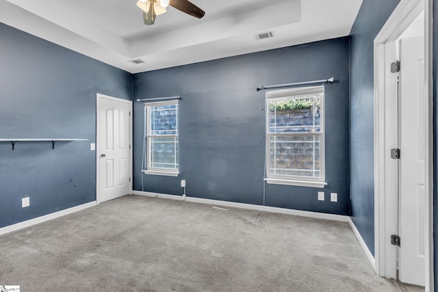 unfurnished room with a raised ceiling, light carpet, and ceiling fan