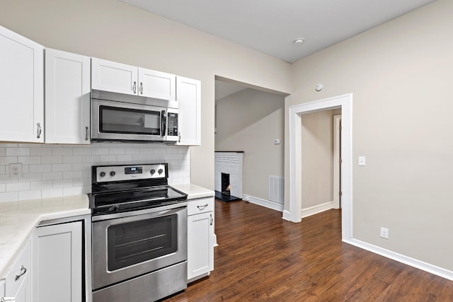 kitchen featuring stainless steel appliances, a brick fireplace, dark hardwood / wood-style flooring, backsplash, and white cabinets