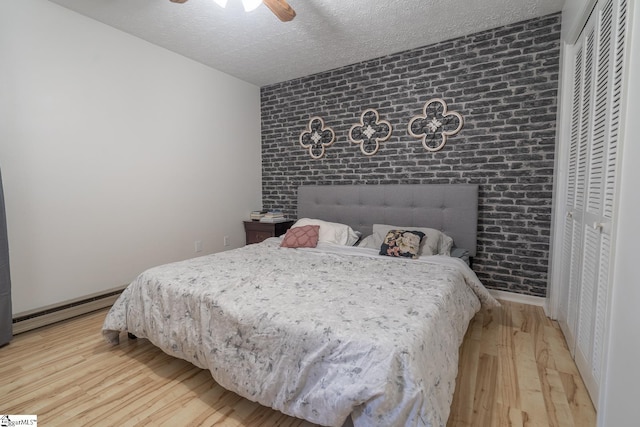 bedroom with ceiling fan, a baseboard heating unit, light hardwood / wood-style floors, a textured ceiling, and a closet