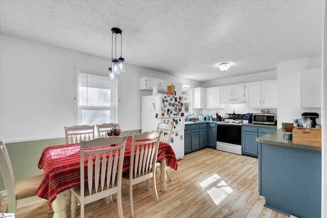 kitchen featuring light wood-type flooring, range with electric cooktop, decorative light fixtures, white fridge, and white cabinetry