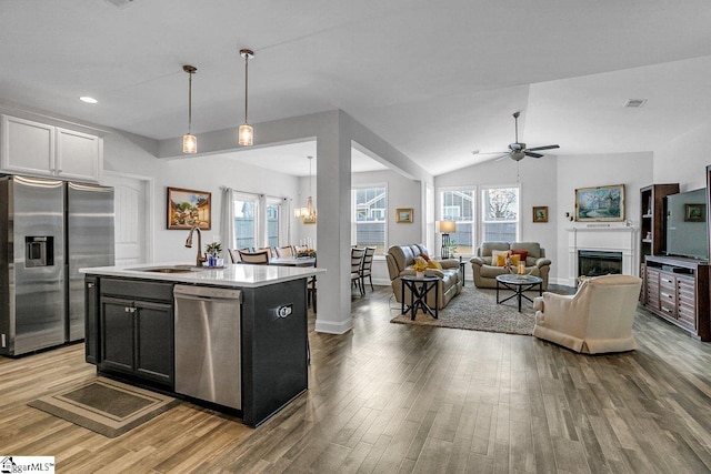 kitchen with an island with sink, wood-type flooring, lofted ceiling, ceiling fan with notable chandelier, and appliances with stainless steel finishes