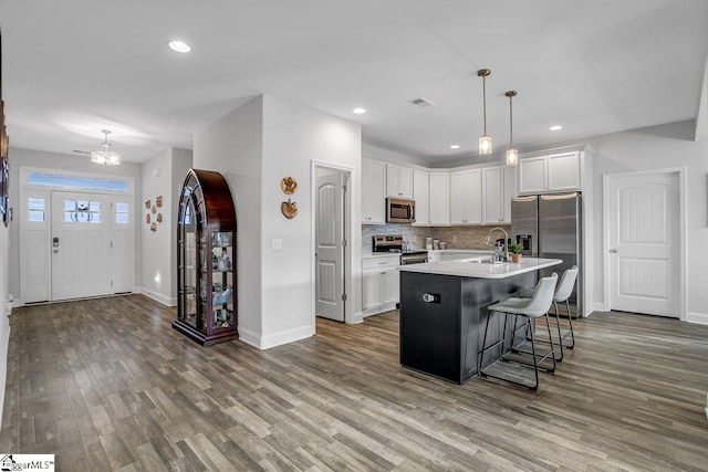 kitchen featuring stainless steel appliances, a kitchen island with sink, hardwood / wood-style flooring, white cabinetry, and hanging light fixtures