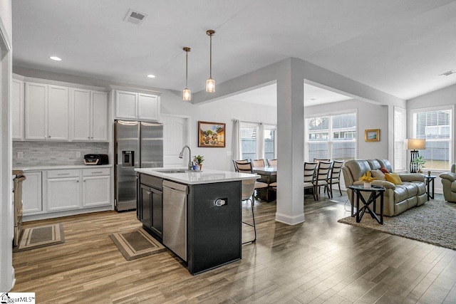 kitchen with a kitchen island with sink, light hardwood / wood-style flooring, decorative light fixtures, white cabinetry, and stainless steel appliances