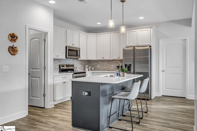 kitchen featuring stainless steel appliances, white cabinetry, a kitchen island with sink, and hardwood / wood-style flooring