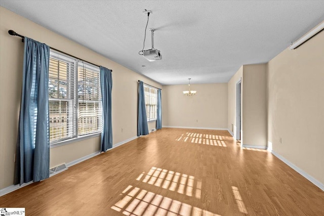 spare room featuring a notable chandelier, light wood-type flooring, and a textured ceiling