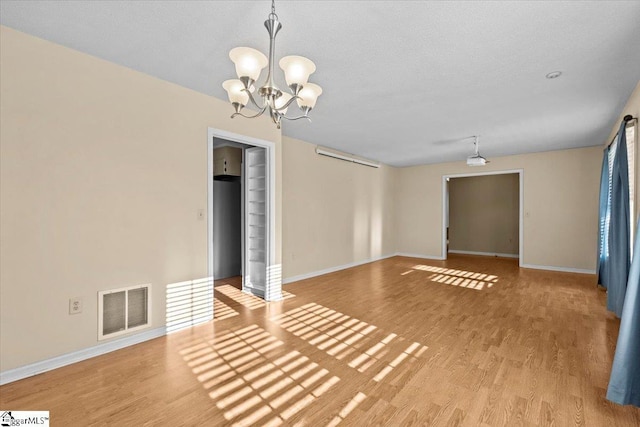 empty room with a chandelier, a textured ceiling, and light hardwood / wood-style flooring