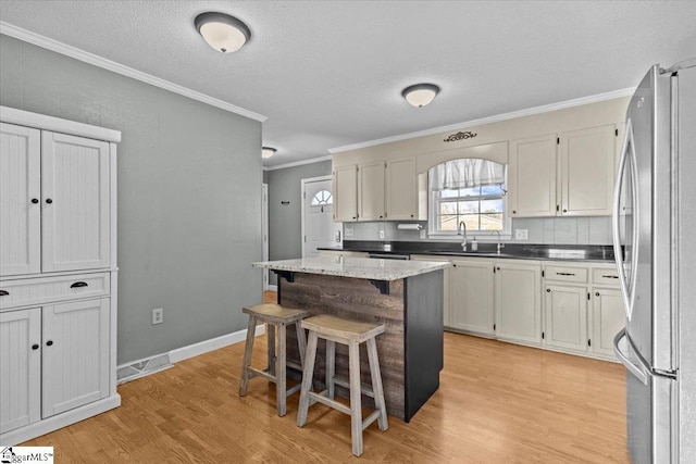 kitchen featuring a kitchen breakfast bar, ornamental molding, a kitchen island, light hardwood / wood-style floors, and stainless steel refrigerator