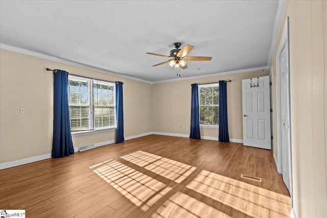 spare room with a wealth of natural light, crown molding, wood-type flooring, and a textured ceiling