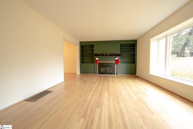 unfurnished living room featuring built in features, hardwood / wood-style flooring, and a brick fireplace