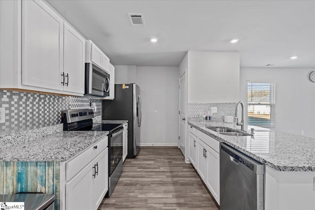 kitchen featuring appliances with stainless steel finishes, light stone counters, sink, hardwood / wood-style flooring, and white cabinetry