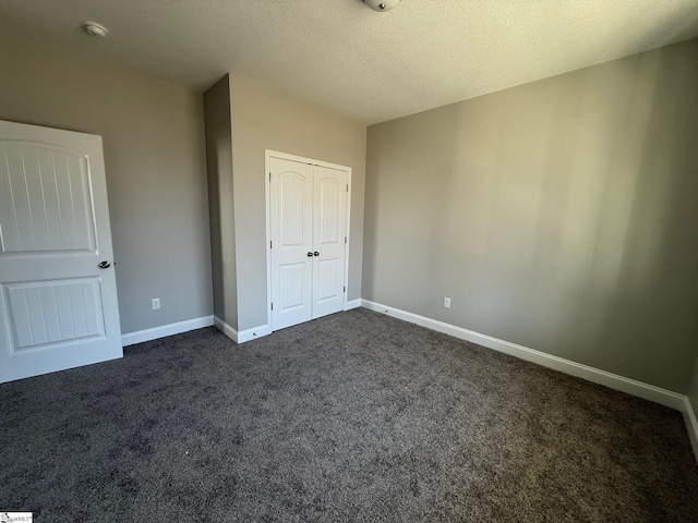 unfurnished bedroom with a textured ceiling, dark carpet, and a closet