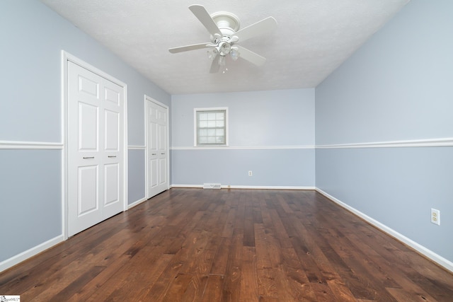 unfurnished bedroom featuring ceiling fan, dark hardwood / wood-style flooring, a textured ceiling, and two closets