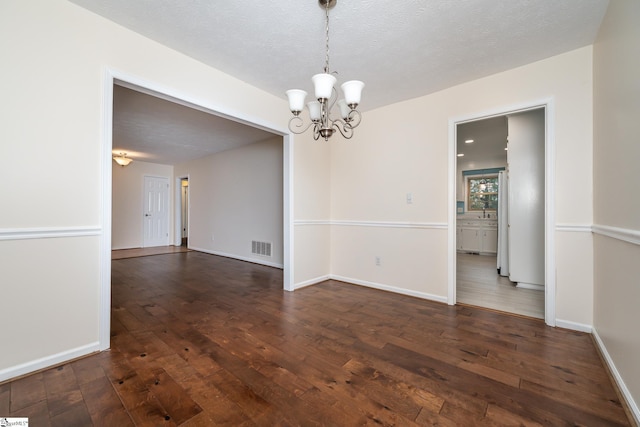 spare room with a textured ceiling, dark wood-type flooring, and a notable chandelier