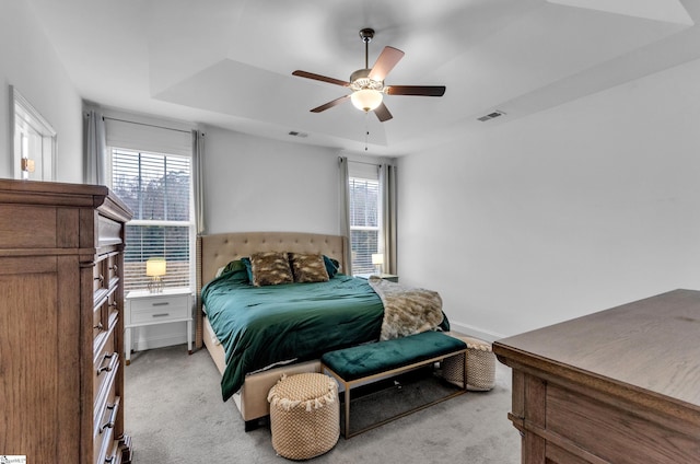 carpeted bedroom featuring ceiling fan, a raised ceiling, and multiple windows