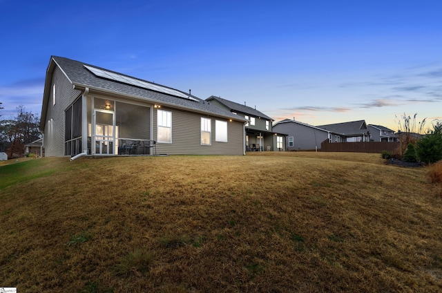 property exterior at dusk featuring a lawn, solar panels, and a sunroom