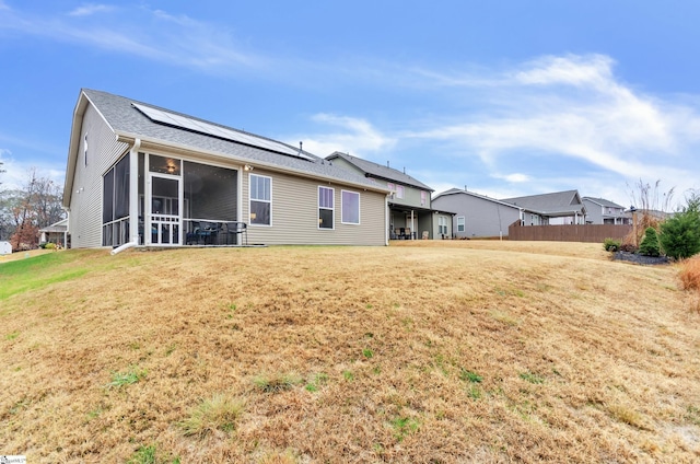 back of property with solar panels, a lawn, and a sunroom