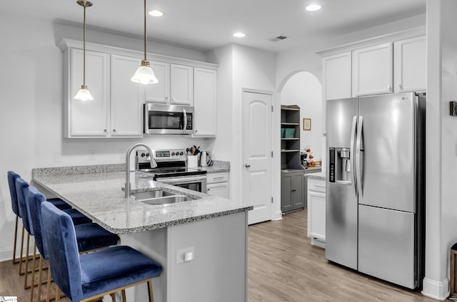 kitchen featuring kitchen peninsula, stainless steel appliances, pendant lighting, light hardwood / wood-style flooring, and white cabinetry