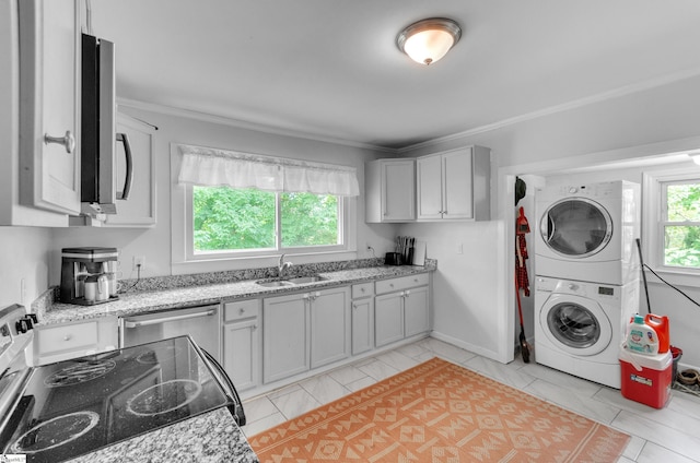 kitchen with stacked washer and dryer, light stone counters, stainless steel appliances, and sink