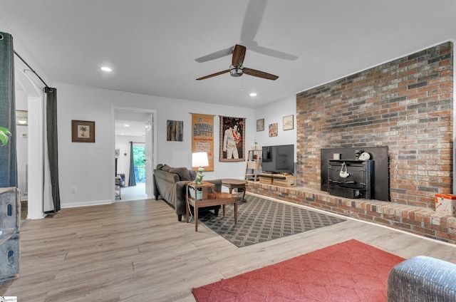 living room featuring ceiling fan, a wood stove, and light hardwood / wood-style flooring