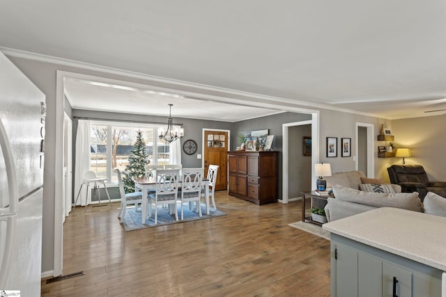 interior space featuring crown molding, white refrigerator, light hardwood / wood-style flooring, a notable chandelier, and hanging light fixtures