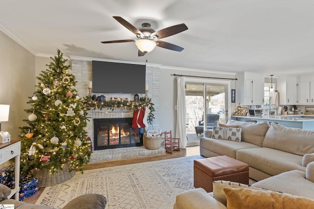 living room with a brick fireplace, light hardwood / wood-style flooring, ceiling fan, and crown molding