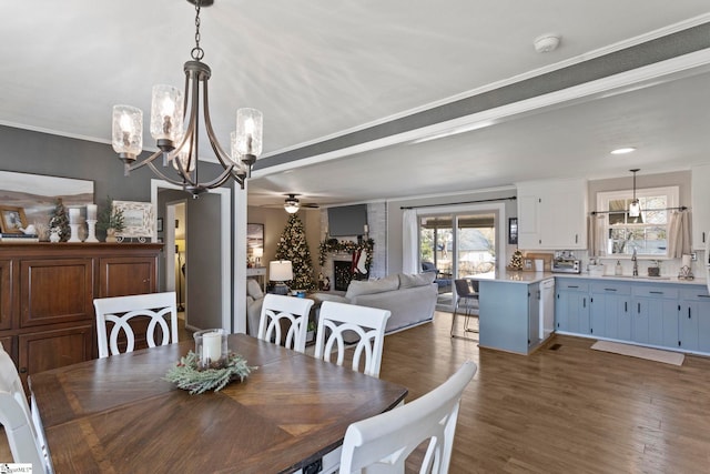 dining room with ornamental molding, ceiling fan with notable chandelier, dark wood-type flooring, sink, and a fireplace