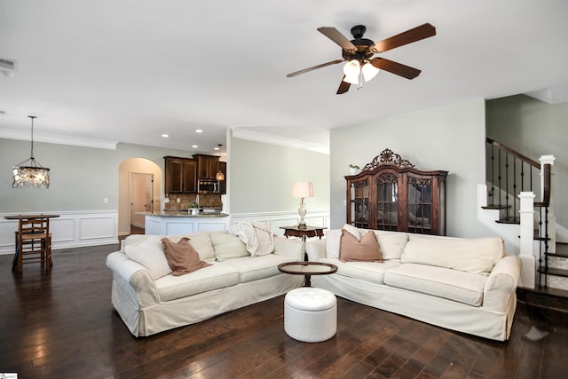 living room with ceiling fan with notable chandelier, crown molding, and dark wood-type flooring