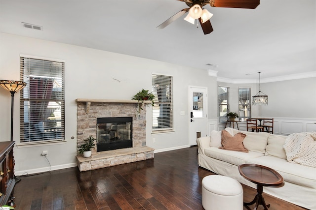 living room with a stone fireplace, ceiling fan with notable chandelier, dark hardwood / wood-style floors, and ornamental molding