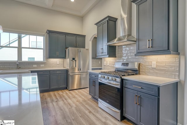 kitchen with stainless steel appliances, wall chimney range hood, backsplash, gray cabinets, and light wood-type flooring