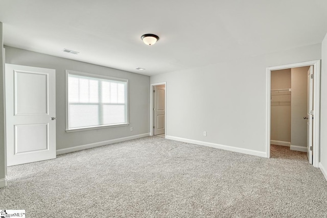 unfurnished bedroom featuring a walk in closet, light carpet, and a closet