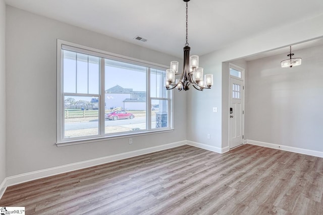 unfurnished dining area featuring a notable chandelier, plenty of natural light, and light wood-type flooring