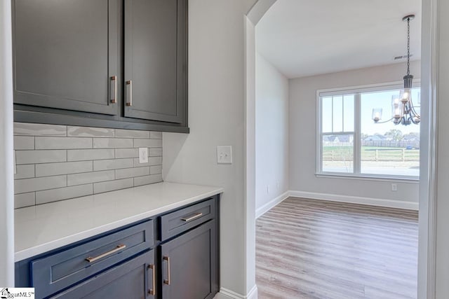 bar with gray cabinetry, decorative backsplash, decorative light fixtures, and light wood-type flooring