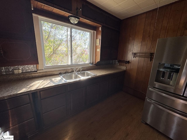 kitchen featuring dark brown cabinets, dark wood-type flooring, sink, stainless steel fridge with ice dispenser, and wood walls