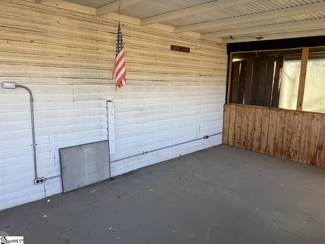 empty room with beamed ceiling, concrete flooring, and wooden walls