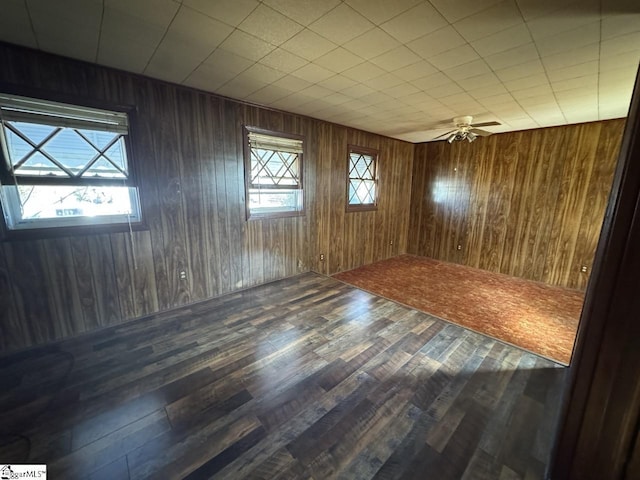 spare room featuring wooden walls, ceiling fan, a healthy amount of sunlight, and wood-type flooring