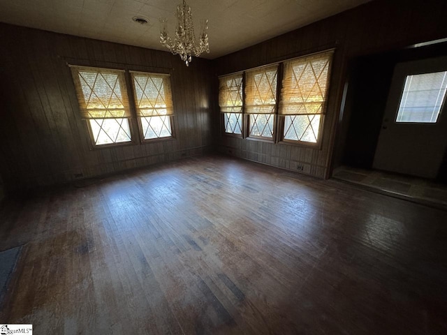 unfurnished dining area featuring a chandelier, dark hardwood / wood-style flooring, a wealth of natural light, and wood walls