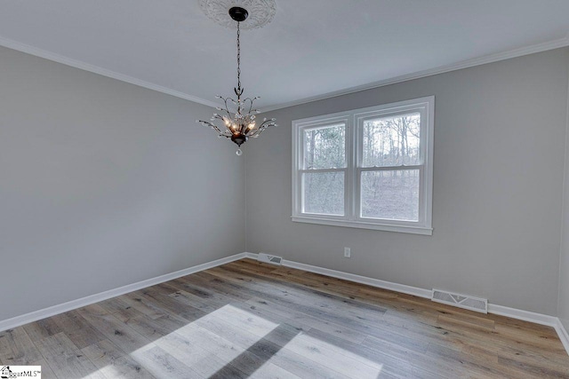 spare room featuring light wood-type flooring, ornamental molding, and a notable chandelier