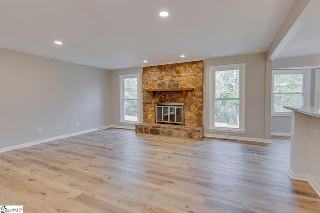 unfurnished living room with light hardwood / wood-style flooring and a stone fireplace