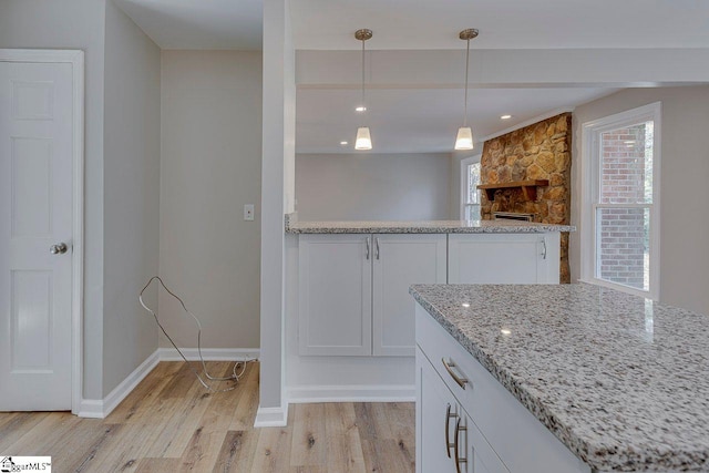 kitchen with white cabinets, pendant lighting, light hardwood / wood-style flooring, and light stone countertops