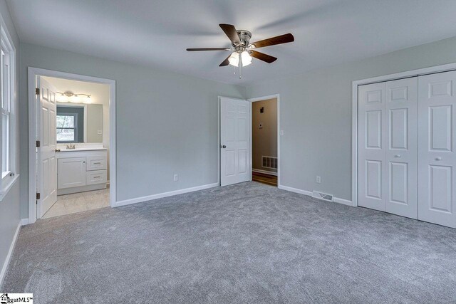 unfurnished bedroom with connected bathroom, ceiling fan, a closet, and light carpet