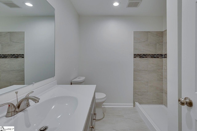 bathroom with tiled shower, vanity, and toilet