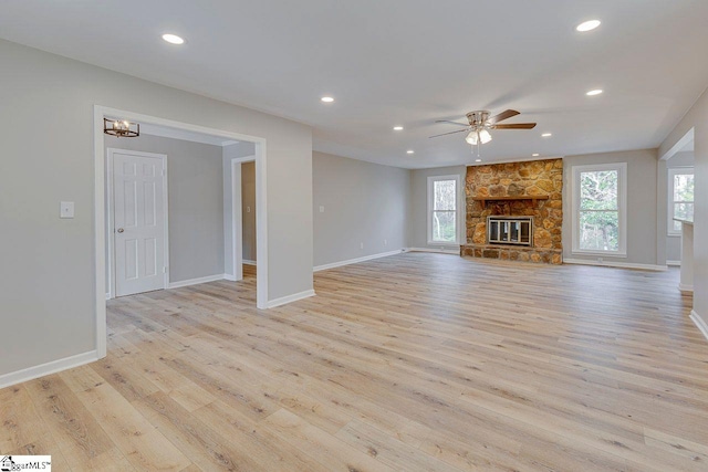 unfurnished living room with light hardwood / wood-style floors, a stone fireplace, and ceiling fan