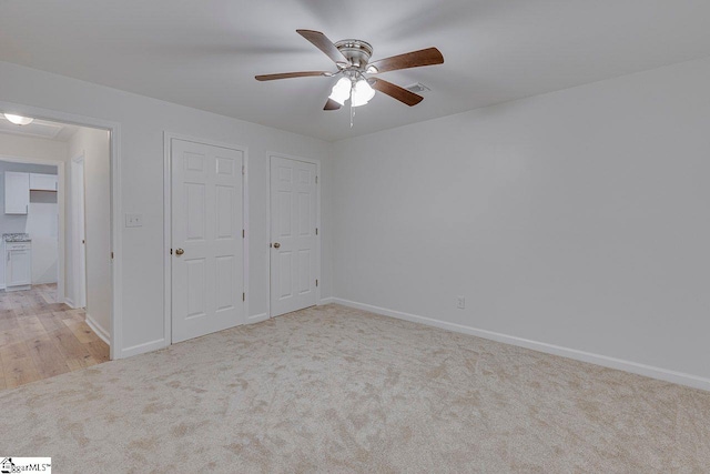 unfurnished bedroom featuring light carpet, ceiling fan, and multiple closets