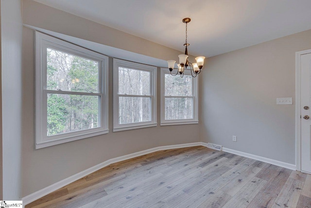 empty room featuring plenty of natural light, a notable chandelier, and light hardwood / wood-style flooring