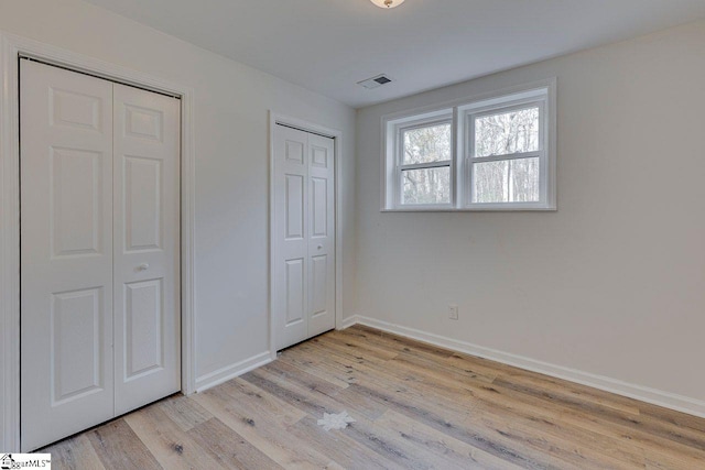 unfurnished bedroom with two closets and light hardwood / wood-style flooring