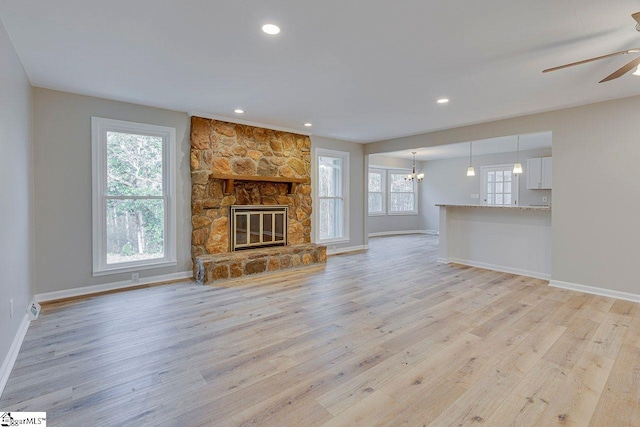 unfurnished living room featuring ceiling fan with notable chandelier, light hardwood / wood-style floors, and a stone fireplace