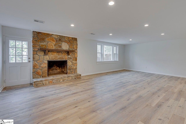 unfurnished living room with plenty of natural light, light hardwood / wood-style floors, and a stone fireplace