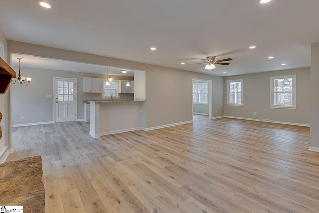 unfurnished living room with ceiling fan with notable chandelier, light hardwood / wood-style floors, and sink