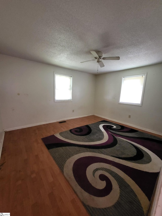 empty room featuring a textured ceiling, hardwood / wood-style flooring, and a healthy amount of sunlight