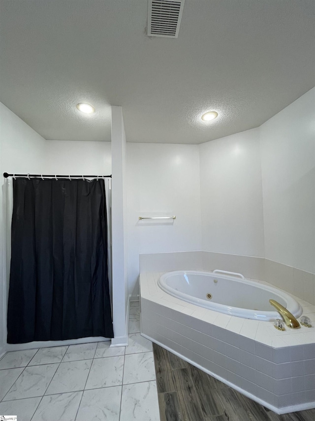 bathroom featuring a textured ceiling and tiled tub